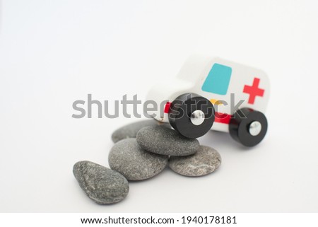Close up of an ambulance, wooden toy, having to deal with stones in its way. Conceptual for adversity, trouble, struggle or crisis