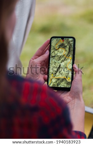 Women hands holding smartphone with app navigation hiking map on screen.  Mountains map with route and markers. Girl planning a trip inside the tent at the camp.  Royalty-Free Stock Photo #1940183923