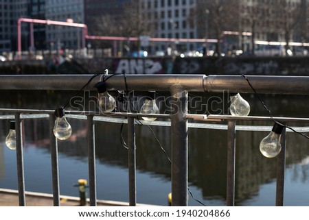 A line of bulbs hanging in a sunny day out of metal rails on a shore of a river for an outdoor party. A light and shadow scenery with blurred background. Stock photography.