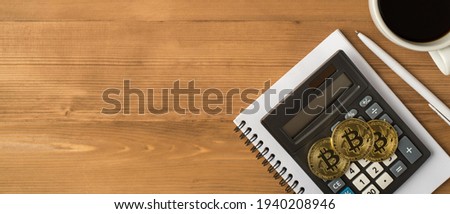 Top view photo of workplace with pen cup of coffee three gold coins with bitcoin symbol and calculator on notebook on isolated wooden table background with copyspace
