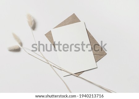 Modern summer stationery still life. Lagurus ovatus foliage and craft envelope. Blank greeting card mock up scene with bunny tail grass isolated on white table background. Flat lay, top view. Royalty-Free Stock Photo #1940213716