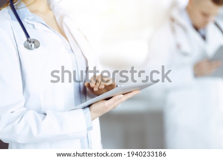 Unknown woman doctor is checking some data at computer tablet, close up. Young doctors at work in a sunny hospital. Perfect medicine and healthcare concept