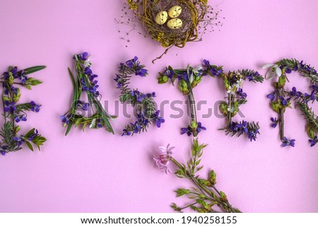  Colorful Easter Greeting Card - word Easter is laid out with first spring flowers and greenery. Flower arrangement is adorned with bird's nest with three small eggs. Flat layout on pink background