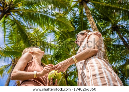 Two women under a palm tree with a coconut in their hands. Jaco beach in Costa Rica