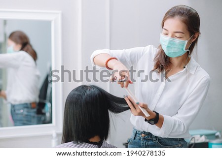 Young Asian woman barber wear green surgical mask, cut black hair customer. Beautiful hairstylist trimming scissors in hair cut salon shop. Female hairdresser with face mask protect working in barber  Royalty-Free Stock Photo #1940278135