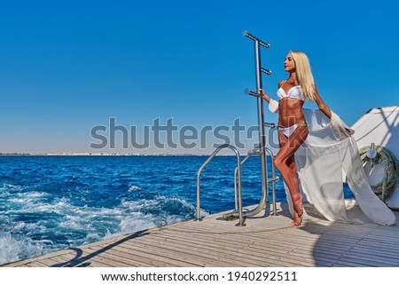 Young woman standing on the deck of a boat in open sea at sunny summer day