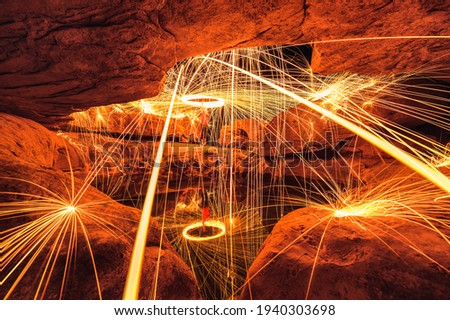 Man wielding spark fire swirl in stone hole cave and pond reflection in the night at Sam Phan Bok, Ubon Ratchathani
