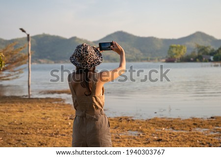 Young asian woman taking a photo by smartphone at mountain lake view in the sunset 