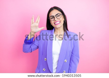 Young business woman wearing purple jacket over pink background doing hand symbol
