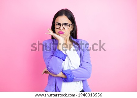 Young business woman wearing purple jacket over pink background thinking looking tired and bored with crossed arms