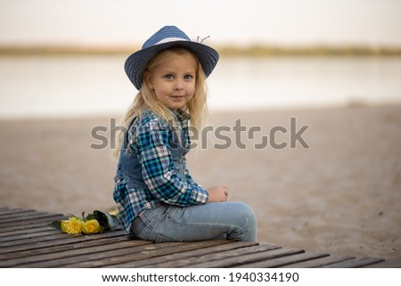 Cute little girl in a hat on the beach with flowers sand