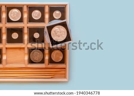 Collection of antique coins in plastic cases in wooden coin album. Numismatist metal coins in transparent cases on blue background. Selective focus Royalty-Free Stock Photo #1940346778