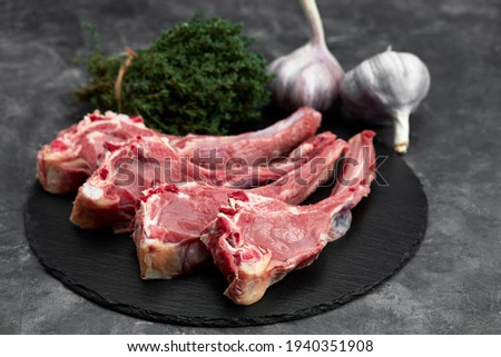 Raw lamb chops with garlic, herbs on black ceramic plate over white stone gray table. Top view. With copy space