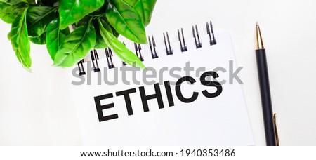 On a white background a green plant, a white notebook with the inscription ETHICS and a pen