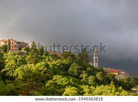 The bell tower of the temple is surrounded by dense vegetation against the backdrop of mountains, low clouds, bright sunlight after rain.