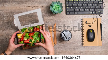 Business lunch at working place. Woman hands taking a photo of healthy take away salmon salad. Notebook smartphone mouse  and succulent on wooden table top view.