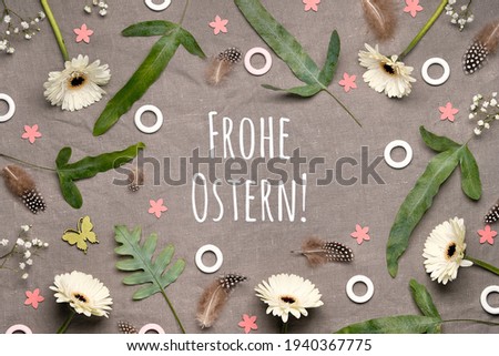 German text Frohe Ostern means Happy Easter. Jungle floral flat lay on linen textile. Bold tropical plant mix. White gerbera flowers, feathers, quail eggs. Natural floral flat lay,