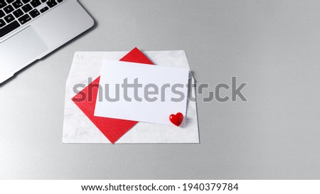 A greeting empty card with an envelope on trendy color 2021 ultimate gray table with laptop. At home or in the office. Valentine day or birthday mockup letter