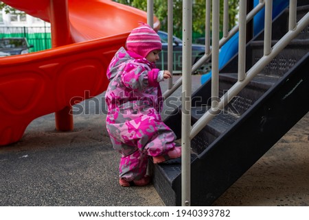 adorable toddler climbs the stairs on the playground. toddler baby dressed in snowsuit. autumn or winter, cold season Royalty-Free Stock Photo #1940393782