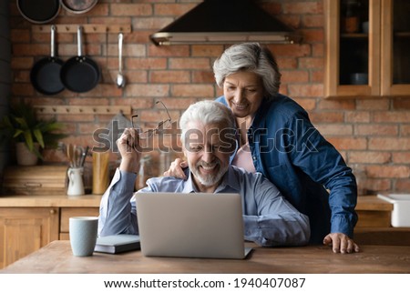No more glasses. Happy elderly man take off eyewear enjoy good sight after laser eye correction. Smiling mature husband sit at kitchen table watch photo in digital family album on pc with beloved wife Royalty-Free Stock Photo #1940407087
