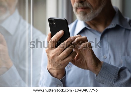 Aged cellphone user. Close up of mature elderly grey bearded casual male hold modern smartphone device in hands text message online use app. Old man retiree surf web chat make call on cell. Copyspace Royalty-Free Stock Photo #1940409796
