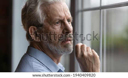 Anxious worried elderly man feel nervous pessimistic look at window wait for someone has mental health problems think of death. Sick abandoned grandpa suffer of loneliness at home in retirement center Royalty-Free Stock Photo #1940409820