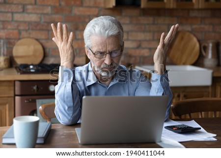 Annoyed worried aged man pensioner sit by laptop unable to make utility bill loan payment online has question how to use app need help. Stressed old grandpa confused with unexpected debt on pc screen Royalty-Free Stock Photo #1940411044