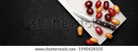 Cherry Tomatoes And Knife On White Cutting Board. Assorted Plum Cherry Tomatoes On Wooden Cutting Board. Scattered Red, Yellow And Black Plum Cherry Tomato On Black Grunge Background.