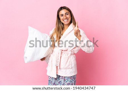 Young hispanic woman over isolated pink background in pajamas and smiling while showing victory sign