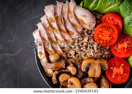 bowl of healthy quinoa with grilled chicken and vegetables on a dark rustic background.