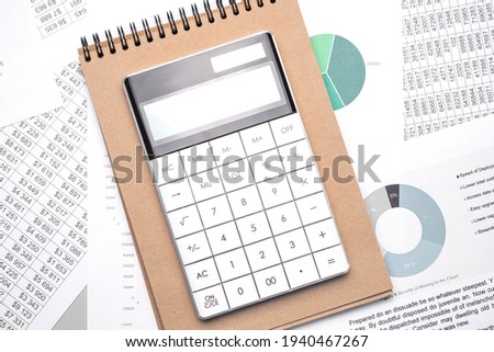 Calculator and an empty Notepad page on the office Desk with financial indicators and charts. Top view with a copy of the text input space.
