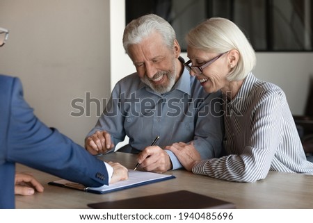 Excited mature Caucasian couple clients sign paper contract with real estate agent or broker buy house together. Smiling older man and woman spouses put signature make health insurance agreement.