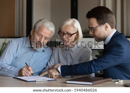 Middle-aged couple clients put signature on paper document make agreement with realtor or broker at meeting. Senior man and woman spouses sign contract close deal buy health insurance.