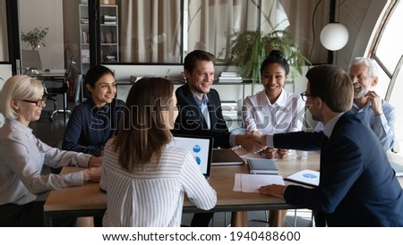 Smiling male colleagues coworkers shake hands close deal at meeting with multiracial employees in office. Businessmen handshake get acquainted greeting making business agreement. Partnership concept. Royalty-Free Stock Photo #1940488600