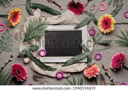 Jungle floral flat lay, linen textile. Blackboard, chalk board with copy-space. Tropical plants, with burgundy, orange, white gerbera flowers, feathers, quail eggs. Flat lay, exotic fern leaves.