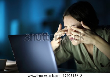 Fatigued woman with eyestrain scratching eyes using laptop late hours in the night at home  Royalty-Free Stock Photo #1940515912
