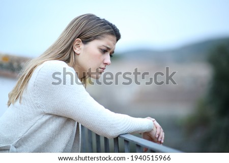 Sad woman looking down in a house balcony complaining alone in a town Royalty-Free Stock Photo #1940515966