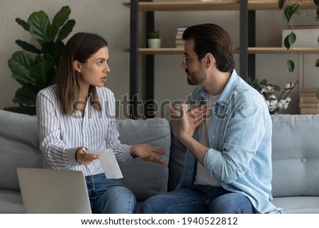 Angry wife and husband quarreling, arguing about unexpected debt or expenses, high domestic bills, sitting on couch with laptop and financial documents, receipts, bankruptcy and money problem concept Royalty-Free Stock Photo #1940522812