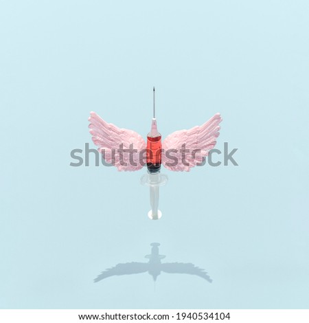 Syringe with needle and pink angel wings against sky blue background. Covid-19 vaccine layout. Creative corona pandemic concept.
