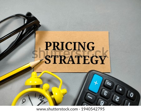 Business concept.Text PRICING STRATEGY with clock,glasses,calculator and pencil on gray background.