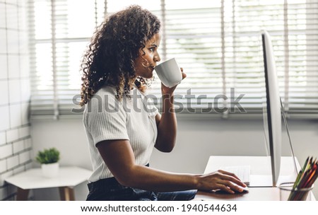 Portrait of smiling happy african american black woman relaxing using technology of desktop computer while sitting on table.Young creative african girl working and drink coffee at home.work from home