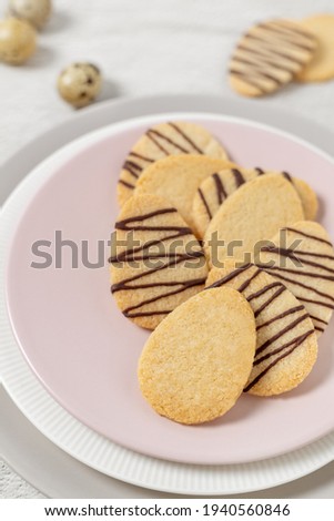Almond butter egg shaped biscuits arranged on round pink plate, chocolate coated Easter sweet treats baked at home with kids, cookies cut in eggs shape front view