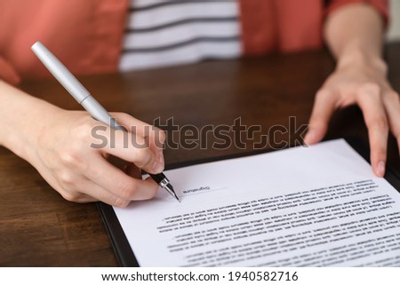 Woman holds pen and signs agreement contract on the table.