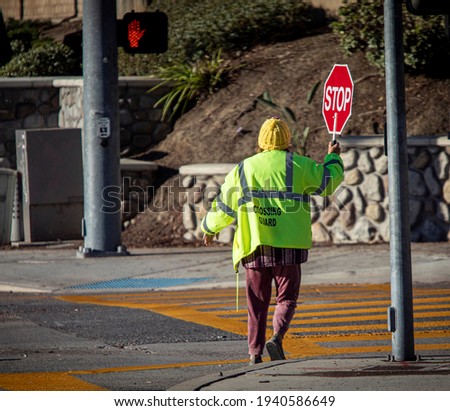 A school crossing guard holding a red stop sign while walking accross a street
