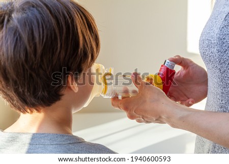 A caucasian woman is giving emergency asthma medication to a small kid during an attack. She uses aerosol chamber with valve mask to deliver bronchodilators or corticosteroids to relieve symptoms. Royalty-Free Stock Photo #1940600593
