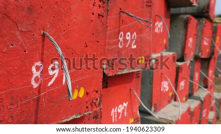 Ground wire in electric poles. A pile of red concrete poles with an embedded anti-short circuit cable with a serial number and a copy area. Select the subject and focus closer.