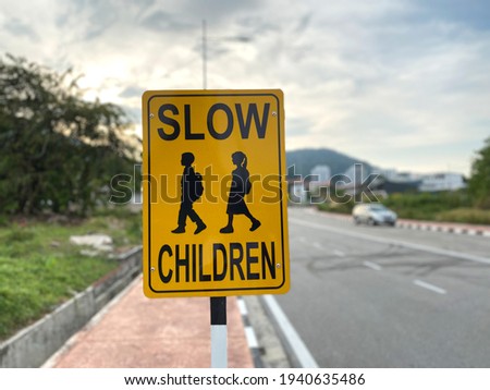 Close up view of a yellow road sign with "SLOW CHILDREN" which reminds vehicles to reduce speed due to school children