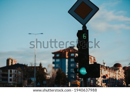 A closeup shot of a traffic light on the green with a timer and a priority road sign during sunset