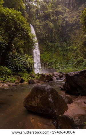Waterfall landscape. Beautiful hidden waterfall in tropical rainforest. Foreground with big stones. Slow shutter speed, motion photography. Travel and adventure. Nung Nung waterfall, Bali, Indonesia
