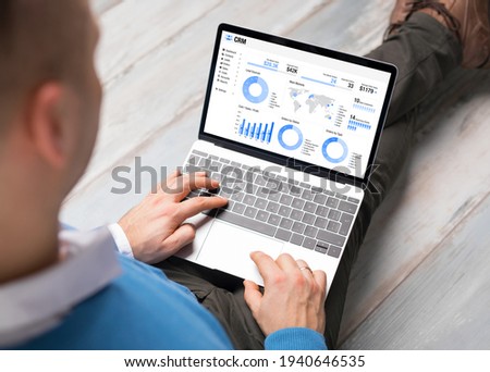 Man using CRM software on laptop with different graphs and charts showing sales data for his business Royalty-Free Stock Photo #1940646535